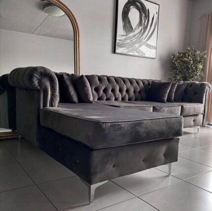 “L-shaped button couch in grey fabric with deep tufting, plush cushions, and a sturdy wooden frame, placed in a modern living room setting.”
